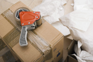 Picture of Moving supplies: duct tape dispenser on top of sealed cardboard box, paper on floor, close-up